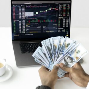 Hands holding cash in front of a laptop displaying stock market data, symbolizing financial growth and investment.