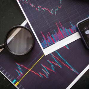 Stock market charts analyzed with a magnifying glass and calculator for financial research.